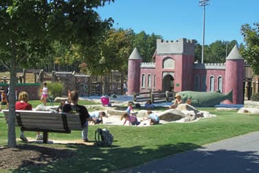 Families gathering beside the castle-themed playground and shaded lawn at Martha Rivers Park