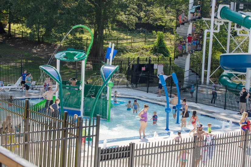 Families using the shallow children's pool and interactive water features at Holding Park Aquatic Center